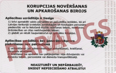 KNAB amatpersonas apliecības reverss. Apliecība ir balta ar sarkanīgām līnijām. Apliecības augšā, vidū ar lieliem melniem burtiem "Korupcijas novēršanas un apkarošanas birojs", zem tā aprakstītas apliecības uzrādītāja tiesības. Pa labi josla ar pelēkiem burtiem "KNAB" un Latvijas valsts ģerbonis. Ar lieliem burtiem pāri apliecībai "PARAUGS".