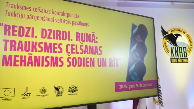 Attēlā redzams liels prezentācijas ekrāns ar dzeltenu fonu, uz kura latviski rakstīts pasākuma nosaukums “Redzi. Dzirdi. Runā: trauksmes celšanas mehānisms šodien un rīt”. Labajā pusē redzams attēls ar luksoforu, bet fonā – Korupcijas novēršanas un apkarošanas biroja emblēma un Latvijas karogs. Ekrāna apakšā atrodami organizatoru un ES fondu logo, kā arī norādīts datums “2025. gada 9. decembris”.