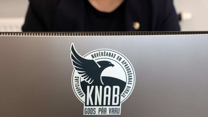 Attēlā redzams dators ar KNAB logo