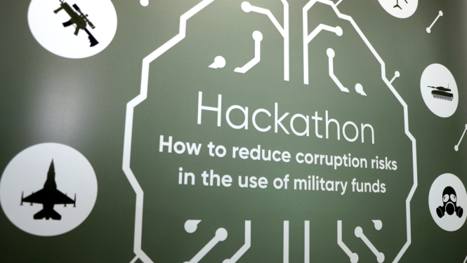 Zaļš fons, vidū uzraksts "Hackathon: How to reduce corruption risks in the use of military funds", apkārt balti apļi ar ikonām, kurās iekļauti pasākuma tematiskās ikonas - lidmašīna, helikopters, tanks, šaujamierocis, gāzmaska.