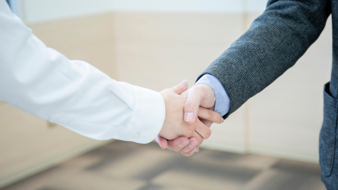 Divu cilvēku rokasspiediens biznesa vidē; redzamas rokas un uzvalki.