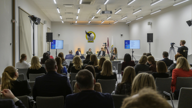 Conference room with the logo of KNAB. Participants sitting facing the logo
