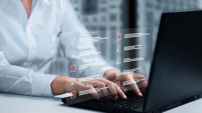 Attēlā redzams cilvēks, kurš raksta uz klēpjdatora tastatūras, bet virs tā redzama caurspīdīga digitāla anketa ar atzīmju rūtiņām, kurās daļa atbilžu ir apstiprinātas ar ķeksīšiem, bet citas noraidītas ar sarkaniem krustiņiem.