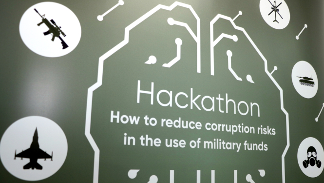 Zaļš fons, vidū uzraksts "Hackathon: How to reduce corruption risks in the use of military funds", apkārt balti apļi ar ikonām, kurās iekļauti pasākuma tematiskās ikonas - lidmašīna, helikopters, tanks, šaujamierocis, gāzmaska.