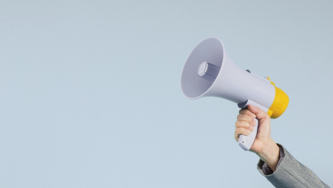 Attēlā redzama personas roka, kas tur skaļruni