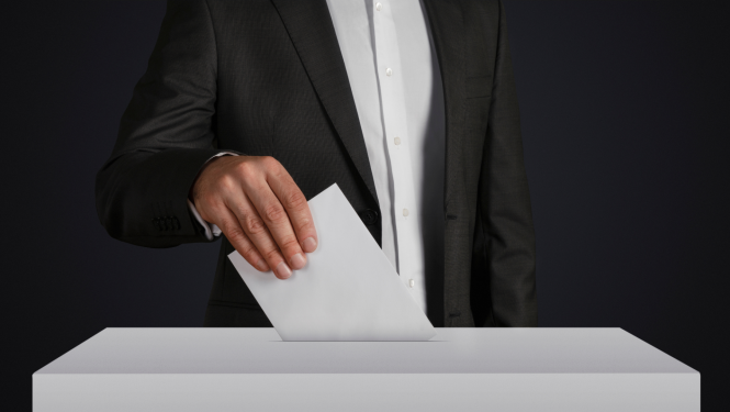 Vīrietis uzvalkā met baltā vēlēšanu kastē baltu aploksni