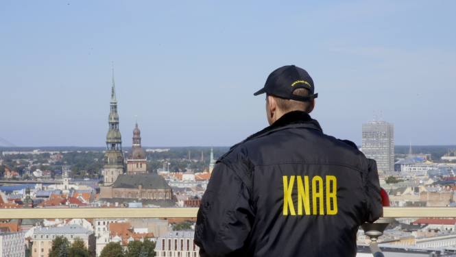 Vīrietis ar jaku, uz kuras izšūts "KNAB"