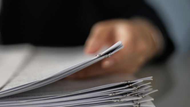 Attēlā redzama cilvēka roka, kas tur dokumentus