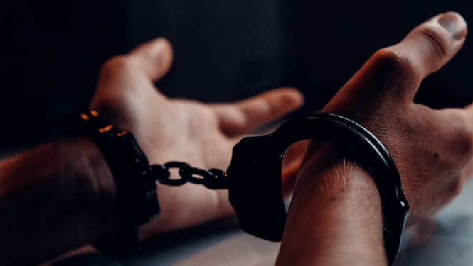 Tumšā istabā vīrieša rokas, kurām uzlikti rokudzelži