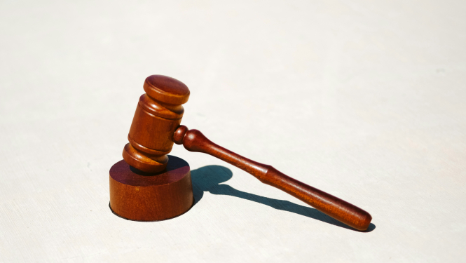 Tiesneša koka āmurs ar pamatni uz gaišas virsmas, simbolizējot likumu un taisnīgumu.